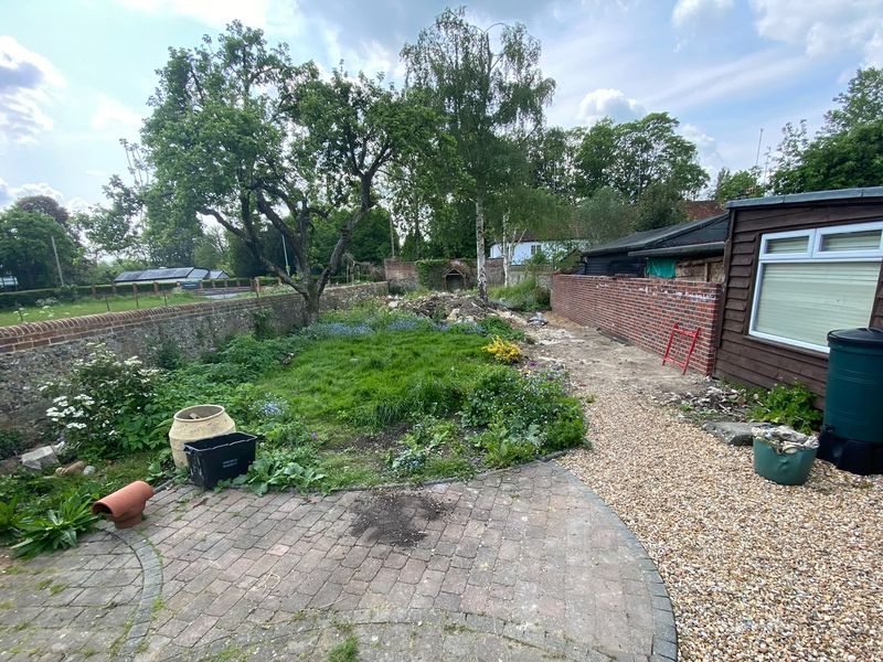 Before &mdash; the walled garden overgrown, weeds through the lawn and worn old block paving beside a gravel path