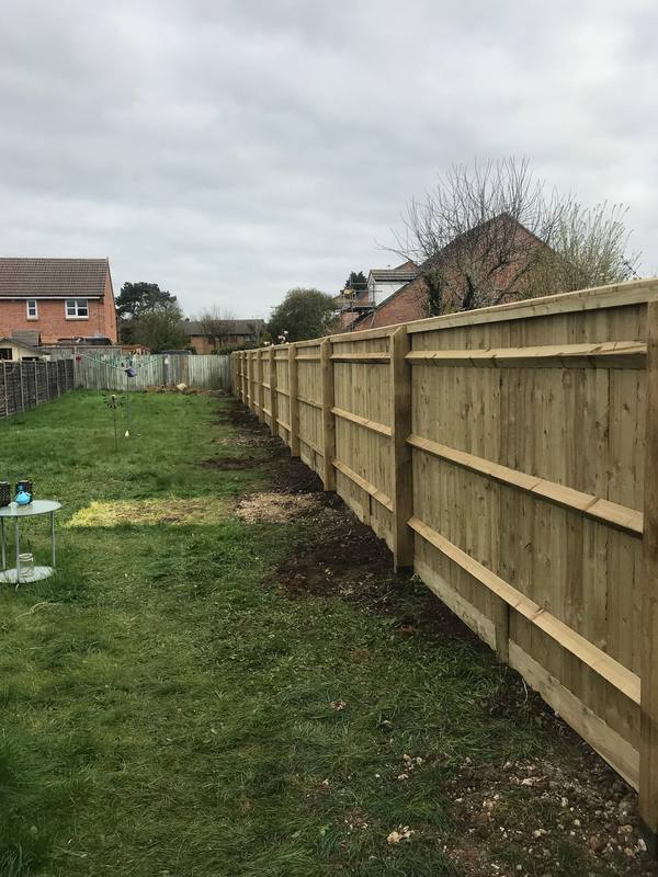 A long closeboard fence on timber posts and rails running beside a lawn