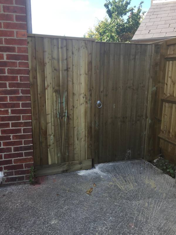A closeboard side gate with a ring latch, between a brick wall and closeboard fencing