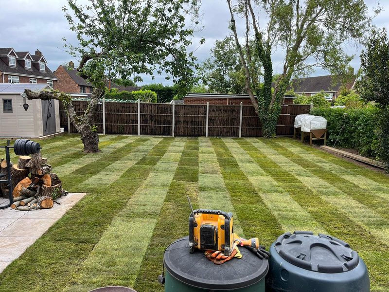 Newly laid turf in alternating strips across a back garden, the roll joins still showing, a site radio in the foreground