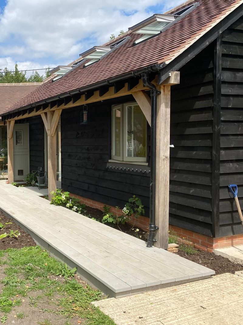 A pale walkway running under the barn's oak-framed colonnade, with new planting either side