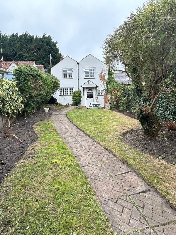 After: the same garden with the grass cut, the herringbone path clear and the borders along the fence dug over, a white house at the end