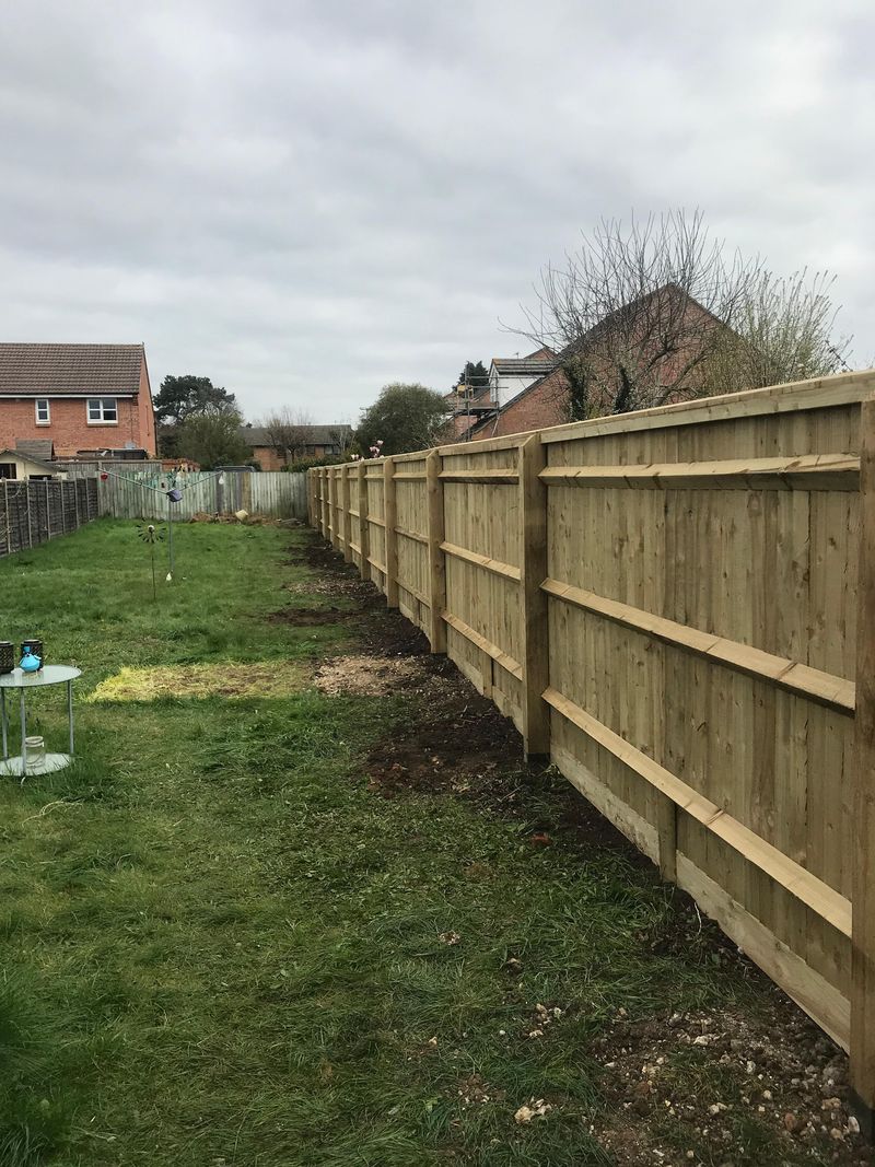 The rail side of the same new closeboard fence seen from the other end of the lawn, with its posts, horizontal rails and gravel boards