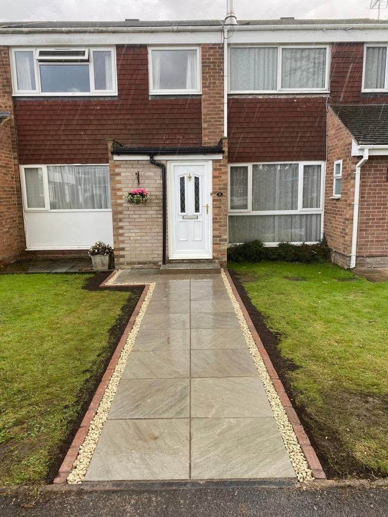 A new front path in grey paving slabs, with a white stone-chipping margin and red-brick edging, running to the front door