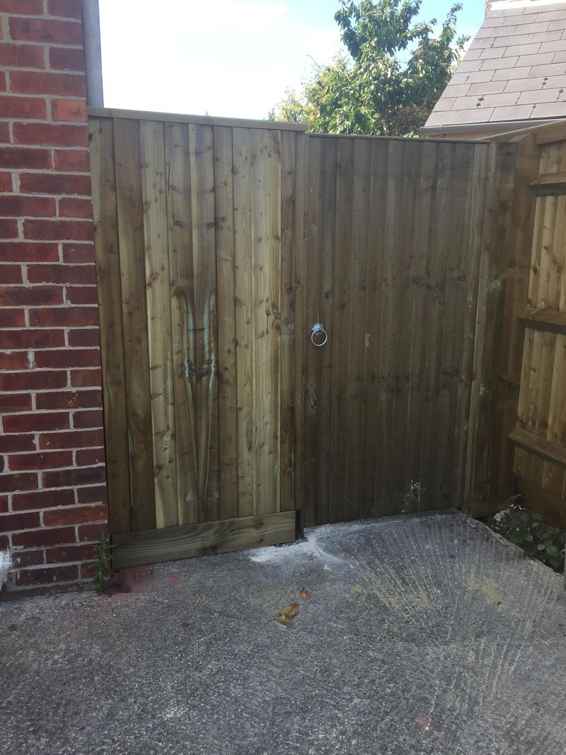 A closeboard side gate with a ring latch, between a brick wall and a closeboard fence above a concrete path